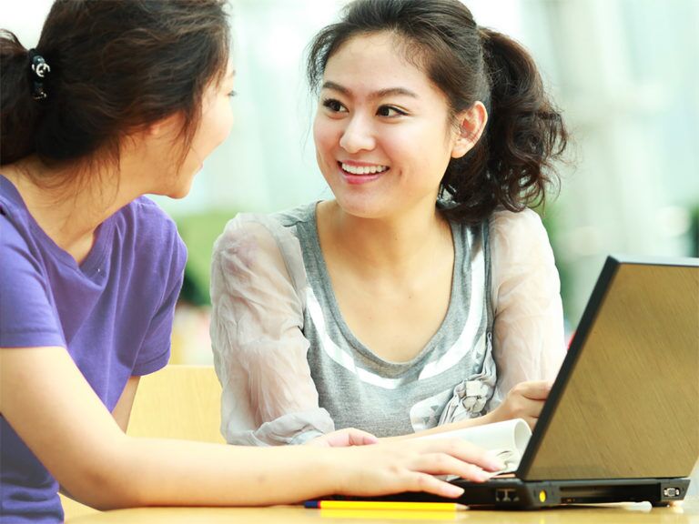 Women smiling in conversation sitting in front of laptop