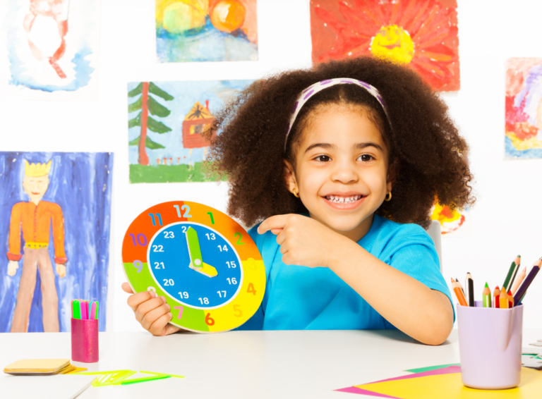 Girl sits at a daycare desk holding a colorful paper clock