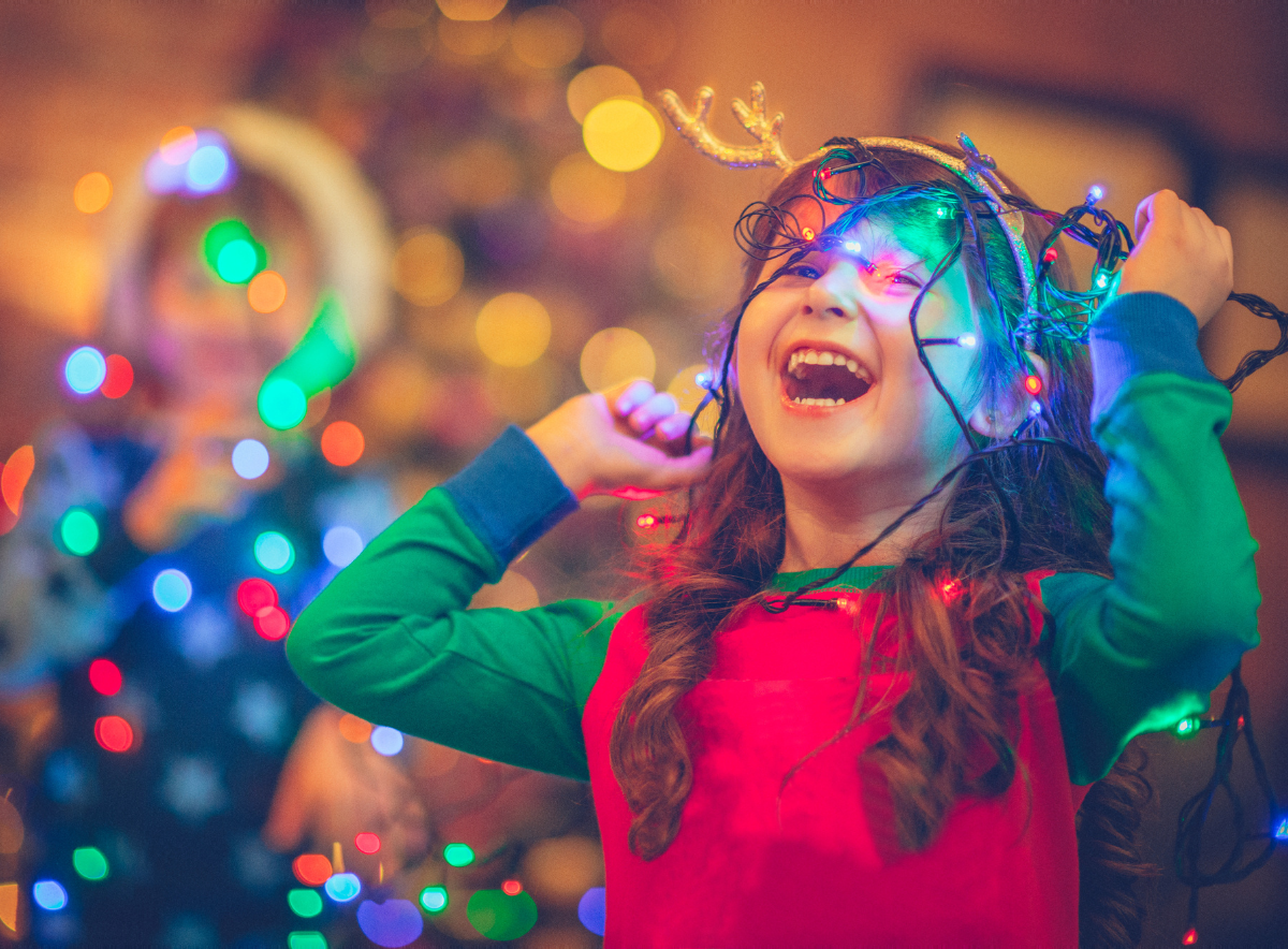 Young girl laughing and playing with holiday lights